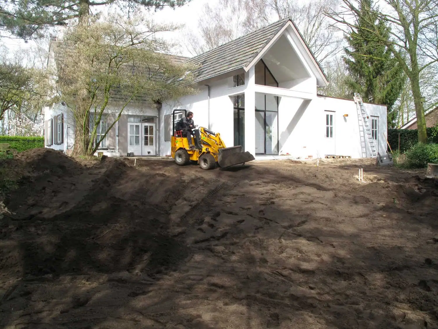 Een gele graafmachine maakt een nieuwe grondhelling in grote tuin