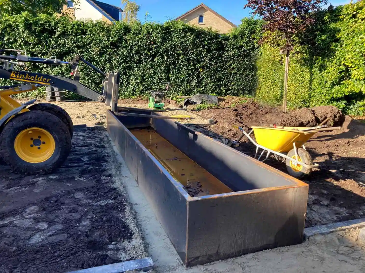 Graafmachine plaatst lange cortenstalen vijverbak in tuin