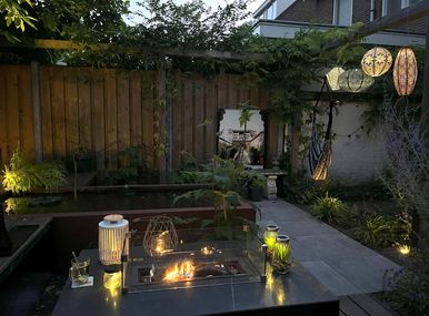 stads-tuinontwerp stads oase in nijmegen van het buitenland met een close up van een verlichte vuurtafel voor een verlichte vijver