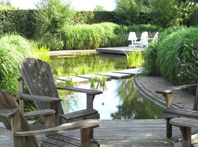 landschaps-tuinontwerp panta rei in nijmegen van het buitenland met een vlonder met loungestoelen die een gebogen vijver begrenst