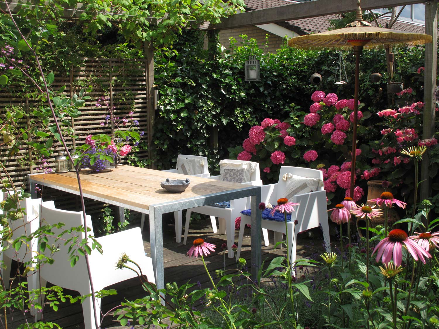 stads-tuinontwerp mozaiek in nijmegen van het buitenland met een buiteneettafel onder een pergola en naast felroze hortensia's