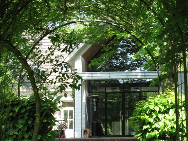 landschaps-tuinontwerp groene oase in nijmegen van het buitenland met een doorkijkje door groene beukenboog naar de veranda